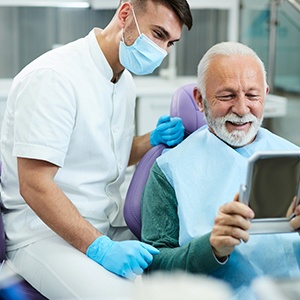 Older man smiling in the mirror at the dentist’s office